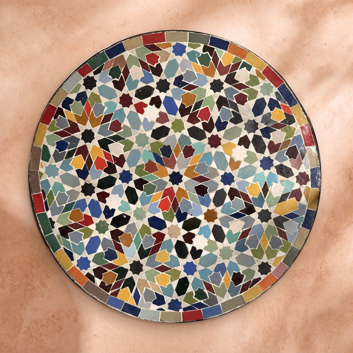 Bahja zellige tabletop seen from above, hand-cut eight-point stars in cobalt, turquoise, green, burgundy, saffron and red with a border of coloured tiles
