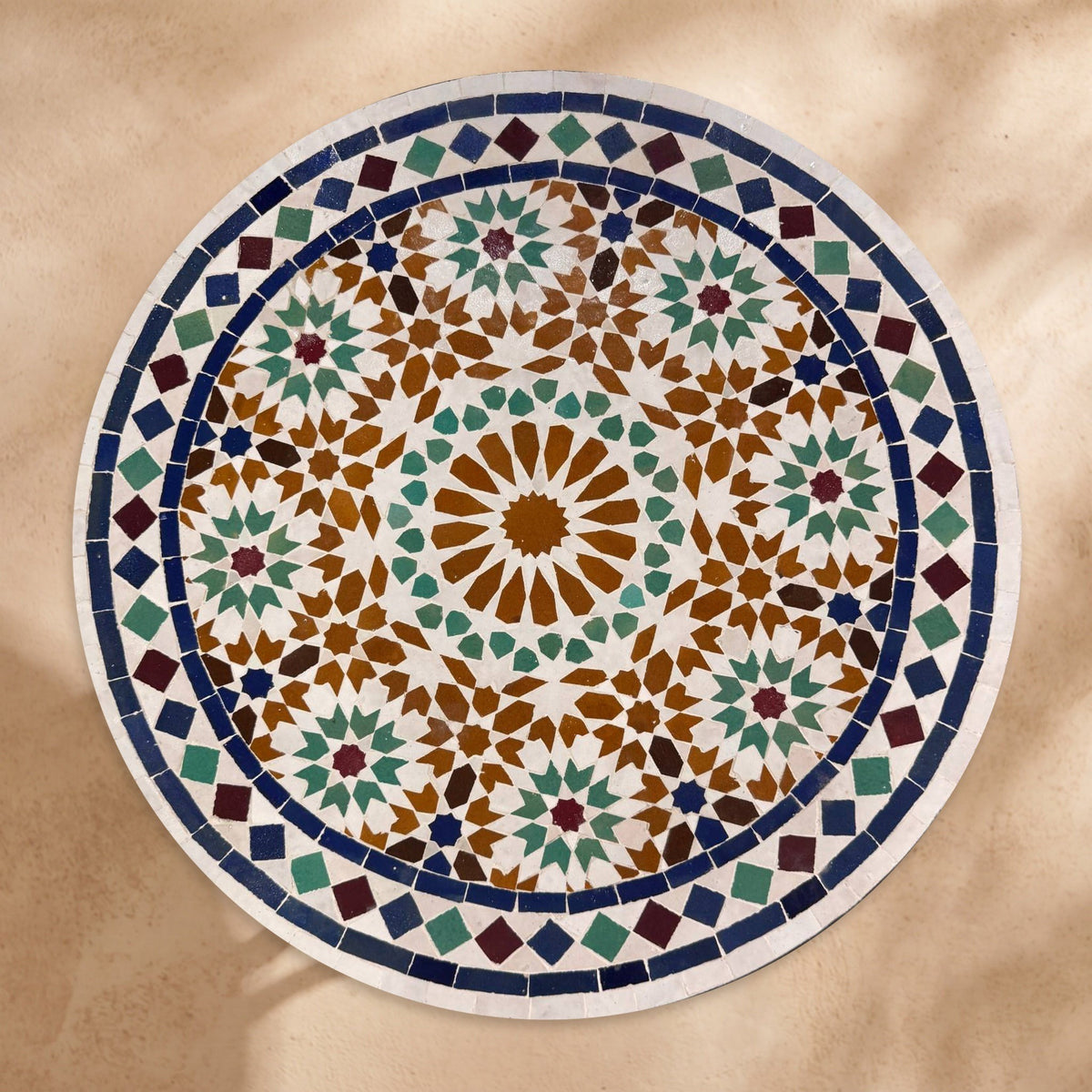 Kawkab handmade Beldi zellige tabletop seen from above, honey amber star ringed by green hexagons and stars inside a navy ring and white diamond border