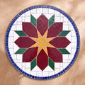 Rbia zellige tabletop seen from above, Rabat lozenge-petal flower in burgundy, ochre and green on white