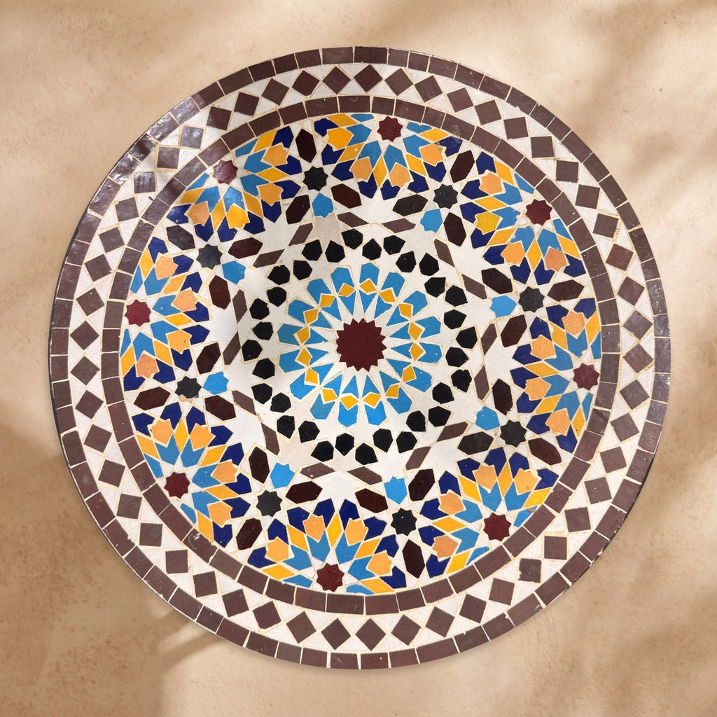 Warda handmade Beldi zellige tabletop seen from above, burgundy sixteen-point star rosette with sky blue, saffron and navy petals inside an aubergine border