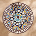 Warda handmade Beldi zellige tabletop seen from above, burgundy sixteen-point star rosette with sky blue, saffron and navy petals inside an aubergine border