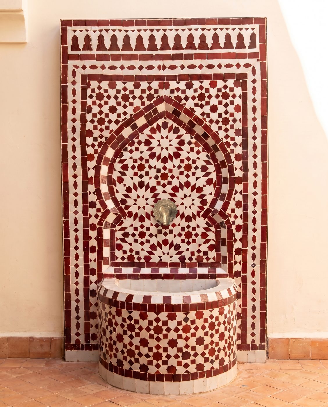 Rot-weißer Zellige-Brunnen in einem cremefarbenen Riad-Hof
